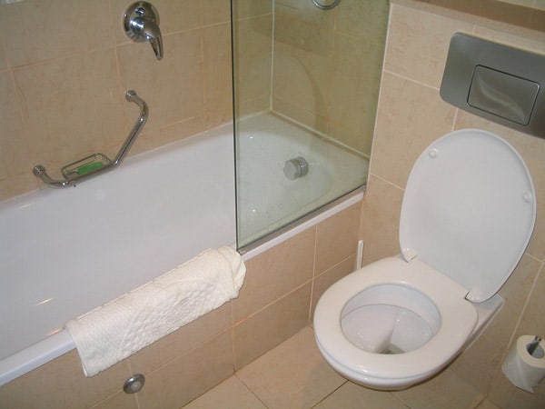 a white toilet in a cream-tiled bathroom next to a white bath tub