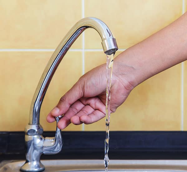 a hand turns off a faucet in a yellow-tiled kitchen