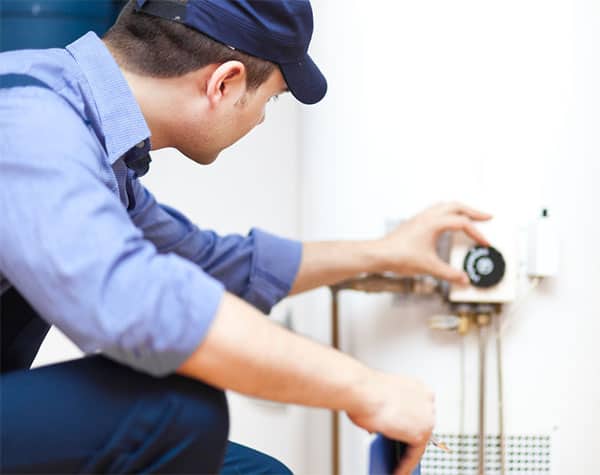 a technician in all blue clothing works on a conventional water heater